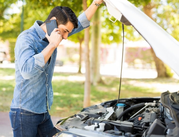 El hombre al teléfono revisa el compartimiento del motor en busca de ruidos de automóviles.