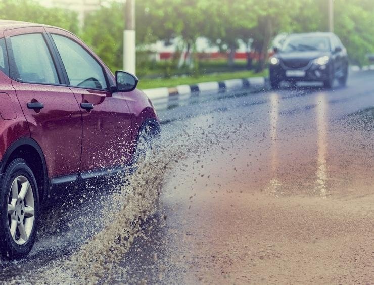 un coche rojo circulando por una carretera mojada